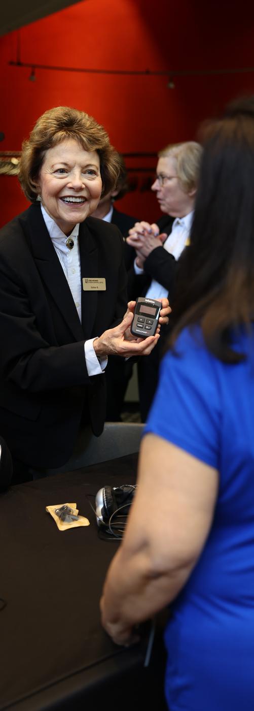 A smiling usher holds up an assisted listening device for a guest